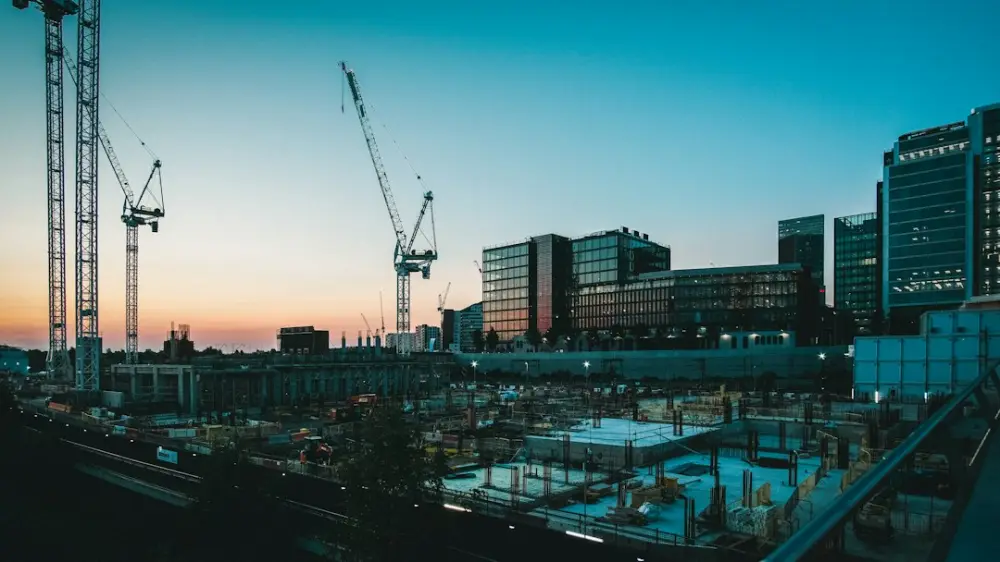 Construction cranes over a building site with concrete foundations at low sun